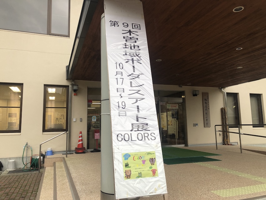 会場 上松町ひのきの里総合文化センター入り口の写真。ボーダレスアート展 COLORSの看板が立てられている。